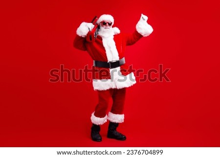 Full size photo of energetic grandfather wear santa costume in glasses hold boombox on shoulder have fun isolated on red color background