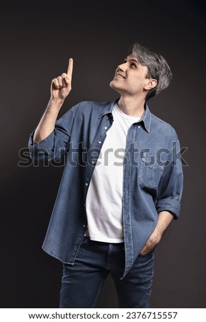 Portrait of Brazilian man, wearing button-down shirt and jeans, smiling and pointing up, gray hair - Color photo - Brazil