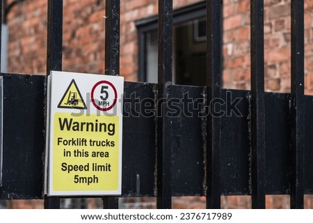 A warning sign attached to a black metal fence indicates the presence of forklift trucks in the area with a speed limit of 5mph.