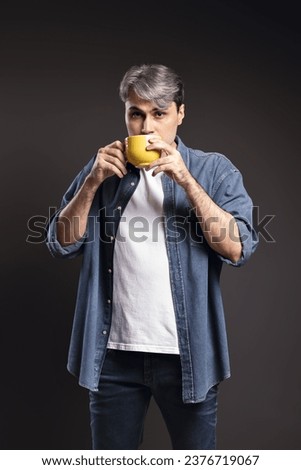 Portrait of Brazilian man, wearing button-down shirt and jeans, with cup, drinking his coffee and looking at camera, gray hair - Color photo - Brazil