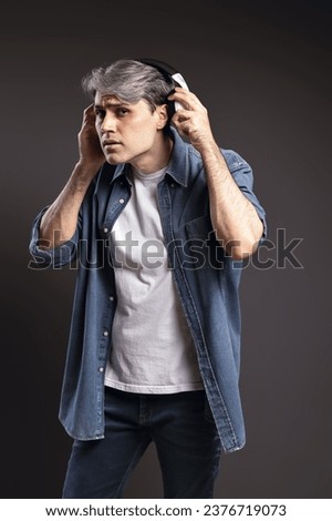 Portrait of Brazilian man, wearing button-down shirt and jeans, taking out headphones to listen to what is being said, gray hair - Color photo - Brazil