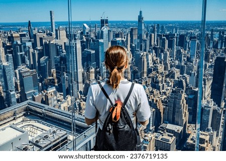 The girl stands facing away on the observation deck of a skyscraper in New York, admiring the view of the city skyline