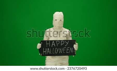 Green screen isolated chroma key photo capturing a creepy mummy holding a black chalkboard with 'happy halloween' written on it. Medium size.