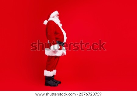Side profile full length photo of santa claus with white beard in sunglass look at logo empty space isolated on red color background