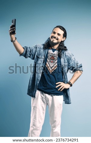Portrait of a Brazilian wearing a button-up shirt and jeans, with one hand on his waist and the other holding his cell phone, smiling, taking a selfie - Belém - Pará - Brazil