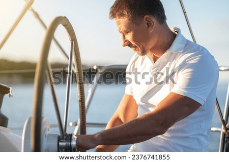Mature fair-haired man holding a rudder of a yacht Royalty-Free Stock Photo #2376741855