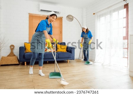 Two Asian young professional cleaning service women worker team working in the house. Girls housekeeper sweeps broomsticks on the wooden floor with another one cleaning under the sofa. Cleaner. Royalty-Free Stock Photo #2376747261