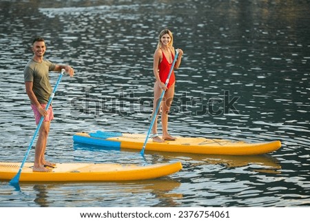 Woman and man surfing in ocean on sup board ar summer vacation. Royalty-Free Stock Photo #2376754061