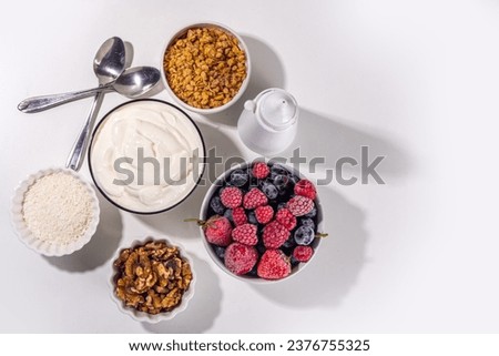 Cooking making Frozen Yogurt Bark background with greek yogurt, fresh berry, granola, honey, chocolate sauce, with baking tray deco. Top view of woman hands cook frozen yoghurt bars