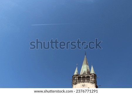 The clock tower at the church in Presov, Slovakia with with green roof and clear blue sky and airplane flying over the city.