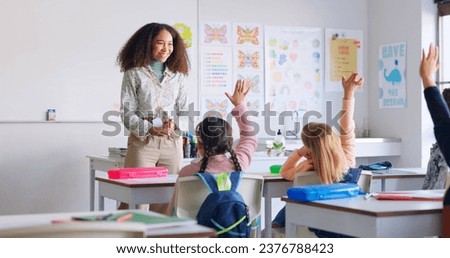 Education, answer and teacher with boy in classroom for learning, discussion and knowledge. Help, studying and hands raised with children and woman at school for why, scholarship and questions Royalty-Free Stock Photo #2376788423
