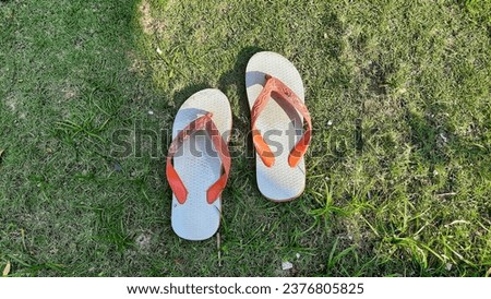 a photo of white and orange flip-flops, photographed with a high angle and green grass background. 