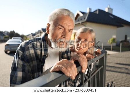 Concept of private life. Curious senior couple spying on neighbours over fence outdoors Royalty-Free Stock Photo #2376809451