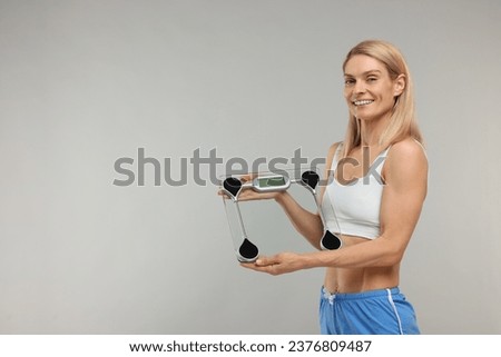 Slim woman holding scales on grey background, space for text. Weight loss