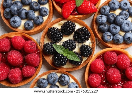 Tartlets with different fresh berries on light table, flat lay. Delicious dessert Royalty-Free Stock Photo #2376813229