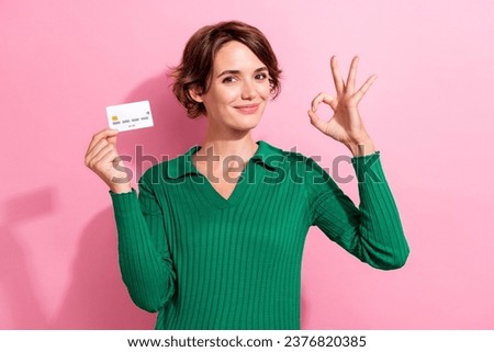 Photo of satisfied girl with bob hairdo dressed green shirt recommend debit card showing okey approve isolated on pink color background