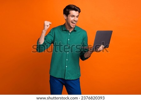 Photo of awesome young guy wear trendy green shirt hold laptop celebrate his promotion career success isolated on orange color background