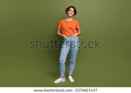 Full length photo of friendly cheerful girl dressed orange t-shirt in eyewear look at offer empty space isolated on green color background