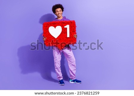 Full size photo of handsome pleasant person dressed violet hoodie hold big red social media like isolated on purple color background