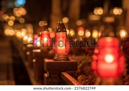 Candle lights on graves and tombstones at a cemetery in Poland during All Saints Day, Zaduszki day, and Day of the Dead. Lit candles illuminate the graves at a Christian cemetery at night. Royalty-Free Stock Photo #2376822749
