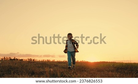Joyful little boy running at sunset. Kid is running across field. Child boy runs through green grass in sun. Childhood dream happiness concept. Happy child playing in nature. Happy family. Dream kid