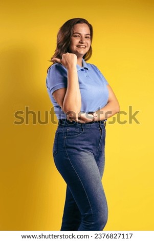 Portrait of a Brazilian woman, wearing a polo shirt and jeans, in three quarter front view, pointing with her thumb, to her right side, smiling and looking at the camera - Belém - Pará - Brazil