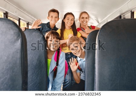 Diverse happy cheerful kids having fun inside a school bus, waving enthusiastically at the camera, smiling pupils posing together, sharing joyful moments during their ride to school Royalty-Free Stock Photo #2376832345