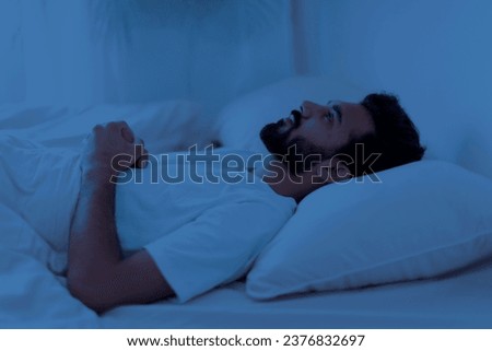 Awake sleepless upset indian man lying in bed alone at night, staring at ceiling, cant sleep, feeling lonely, suffering from depression or anxiety, experiencing difficulties with sleeping Royalty-Free Stock Photo #2376832697