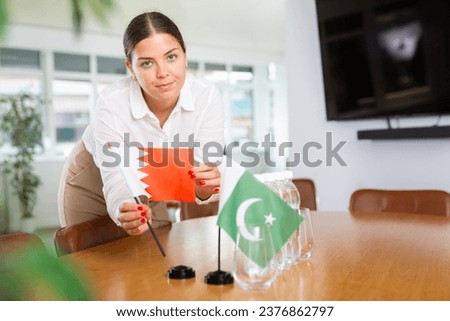 Young woman in business clothes puts flags of Qatar and Pakistan on negotiating table in office