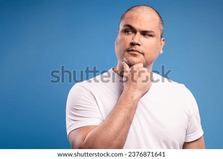 Portrait of a Brazilian man wearing a basic white shirt, in three quarter front view, with his right hand holding his chin, thoughtfully, looking to the side - Belém - Pará - Brazil