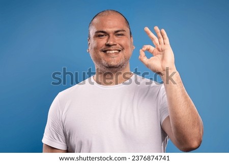 Portrait of a Brazilian man wearing a basic white shirt, from the front, making the OK sign with his left hand, raised to his face, looking at the camera and smiling - Belém - Pará - Brazil