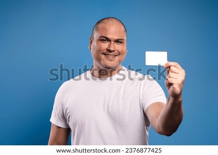 Portrait of a Brazilian man wearing a basic white shirt, facing forward, holding a paper card with his left hand, smiling and looking at the camera - Belém - Pará - Brazil