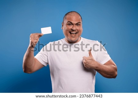 Portrait of a Brazilian man wearing a basic white shirt, facing forward, holding a paper card in his right hand, and giving a thumbs up with his left hand, smiling and looking at the camera - Belém