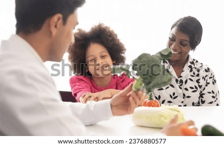 Hispanic nutritionist doctor consulting a young girl child with her African American mother about a nutrition. Vegetables food - a new way for the good healthy and lifestyle. Royalty-Free Stock Photo #2376880577