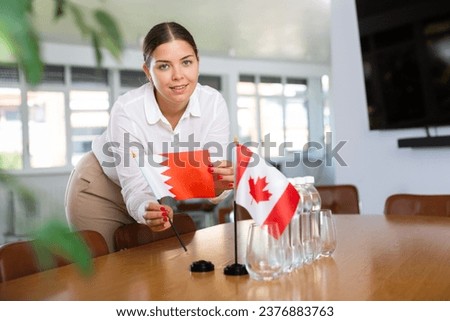 Young woman in business clothes puts flags of Qatar and Canada on negotiating table in office