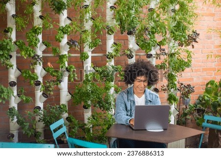 Smiling young ethnic men, dressed in casual clothes, in a green area in nature against the backdrop of a smart garden with modern hydroponic systems. Sustainable environment green space for work  Royalty-Free Stock Photo #2376886313