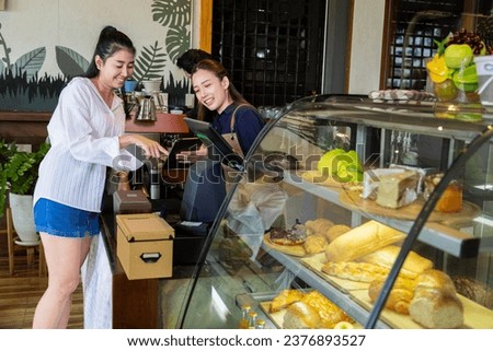 Asian beautiful woman employee wear apron stands at counter taking orders from customers, happy barista recommending new menu, Small business coffee shop owner talk to clients restaurant guests.