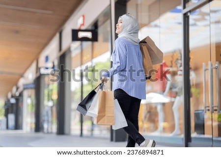 An Asian Muslim woman is carrying a bag of goods that she has been shopping for and buying a lot of products with happy, happy faces.
