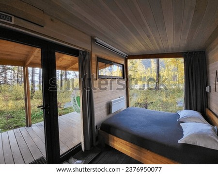 Interior of vacation rental forest lodge countryside cabin with large terrace and big window among trees for holidays in the wilderness. Modern hideaway cottage in wild pine forest on river bank. Royalty-Free Stock Photo #2376950077