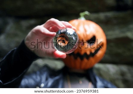 An adult model wearing a pumpkin head mask poses with a lens ball, which portrays her upside down