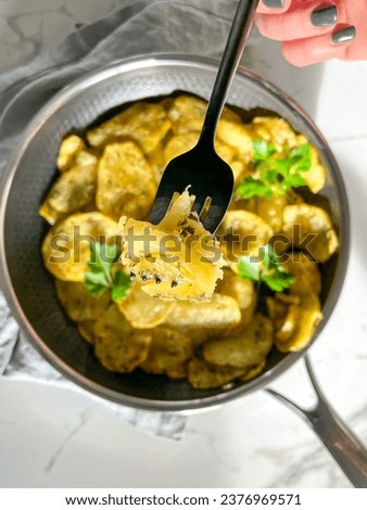 Hand holding fork pf potatoes, Pommes Anna, potato tart in a grey pan with white marble background, parsley, carbs, delicious food photography aerial potato pan picture