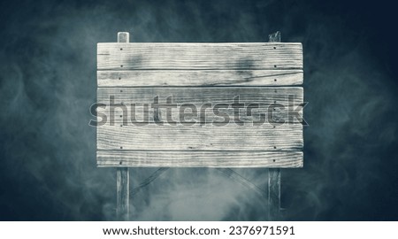 Old rough wooden sign surrounded by fog at night: mystery and horror concept, copy space