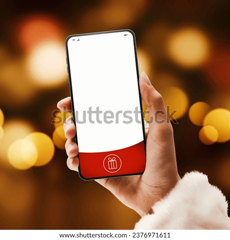 Female Santa Claus holding a smartphone with blank screen and bokeh lights, Christmas and technology concept Royalty-Free Stock Photo #2376971611