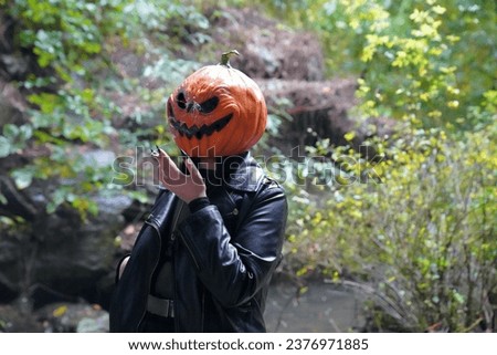 An adult model wearing a pumpkin mask smokes in Central Park on a rainy day