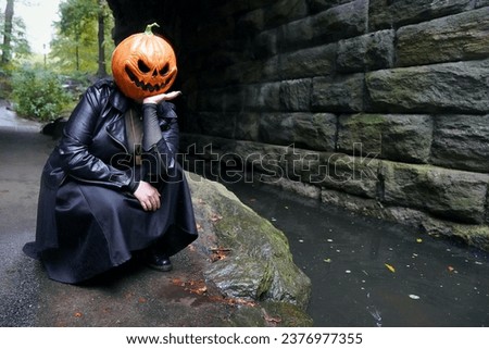 An adult model wearing a pumpkin mask squats next to The Loch stream and poses for a portrait