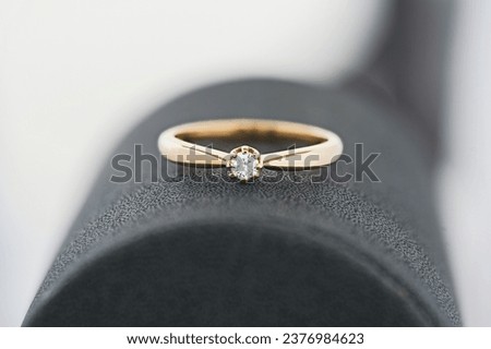 Close-up shot of a sleek gold ring showcasing a solitary diamond, positioned on a textured dark surface with a gentle white gradient background. Royalty-Free Stock Photo #2376984623