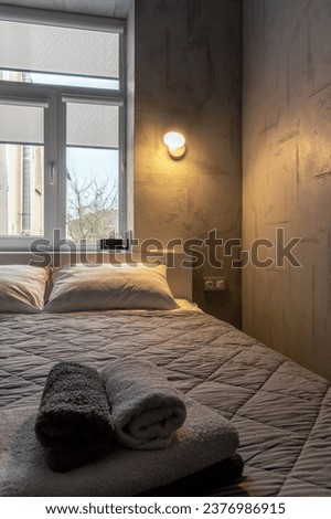 Bed in the bedroom, against the background of the window and glowing sconces on the wall.