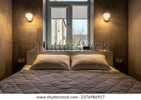 Bed in the bedroom, against the background of the window and glowing sconces on the wall.
