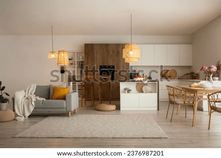 Interior of modern open plan kitchen with dining table, island, grey sofa and glowing lamps Royalty-Free Stock Photo #2376987201