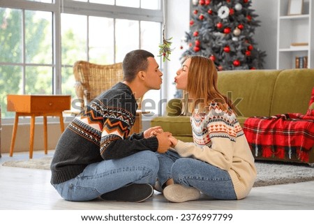 Young couple kissing under mistletoe branch at home on Christmas eve
